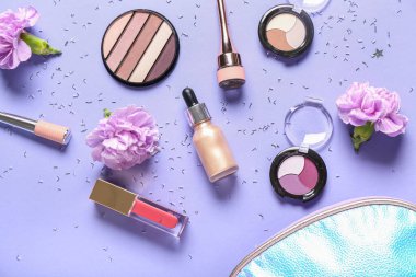 Makyaj ürünleri, çiçekler ve eflatun arkaplanda konfeti bulunan kozmetik çanta.