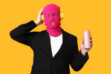 Kulaklıkları ve sarı arka planda bir kutu gazozu olan kar maskeli bir genç.