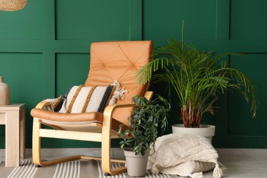 Yastıklı şık bir koltuk, sehpa ve oturma odasındaki yeşil duvarın yanındaki bitkiler.
