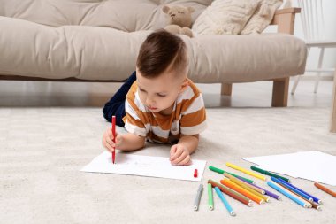 Evinde yerde keçeli kalemlerle çizen sevimli küçük çocuk.