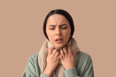 Kahverengi arka planda boğazı ağrıyan fularlı güzel bir kadın.