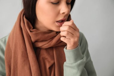 Gri arka planda boğazı ağrıyan fularlı güzel bir kadın.