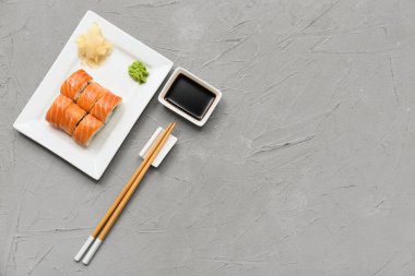 Gri grunge arka planda lezzetli suşi ruloları, yemek çubukları ve soya soslu tabak.