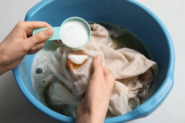 Gri arka plandaki plastik havuza çamaşır deterjanı ekleyen kadın, yakın plan.