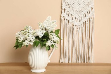 Odadaki bej duvarın yanındaki sehpanın üzerinde çiçek açan dalları olan vazo.