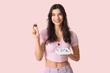 Mutlu genç bir kadın lezzetli çikolata şekerleriyle pembe arka planda kutuda