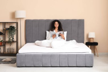 Genç Afro-Amerikalı kadın evdeki yumuşak yatakta dergi okuyor.