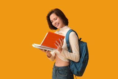 Sarı arka planda not defterleri ve sırt çantasıyla güzel bir kız öğrenci.