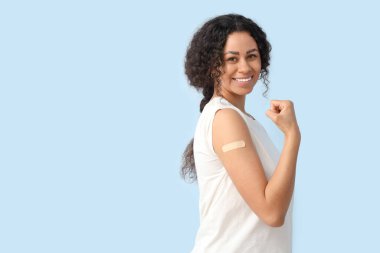 Mavi arka planda aşıdan sonra kaslarını gösteren tıbbi bandı olan genç bir Afro-Amerikalı kadın.