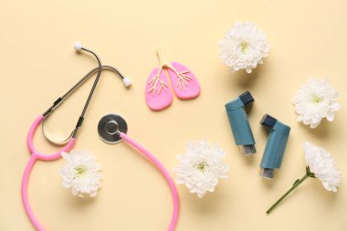 Astım spreyleri, steteskop, akciğer biblosu ve bej arka planda kasımpatı çiçekleri.
