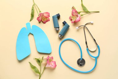 Astım spreyleri, steteskop, kağıt akciğerler ve bej arka planda alstromerya çiçekleri.
