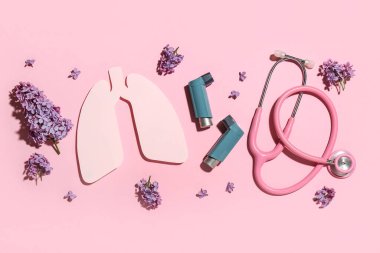 Kağıt ciğerli astım spreyleri, steteskop ve pembe arka planda leylak çiçekleri.