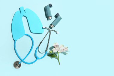 Mavi arkaplanda astım spreyleri, steteskop ve alstromerya çiçeği.