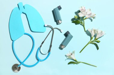 Mavi arkaplanda astım spreyleri, steteskop ve alstromerya çiçekleri.