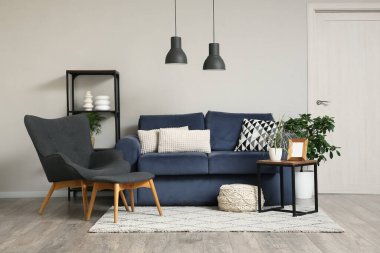 Koltuğu, sehpası ve oturma odasındaki beyaz duvarın yanındaki raf ünitesi olan rahat mavi kanepe.