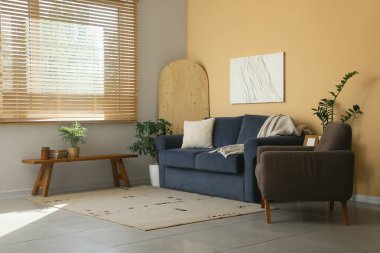 Koltuğu, kahve masası ve oturma odasındaki sarı duvarın yanındaki çiçekli rahat mavi kanepe.