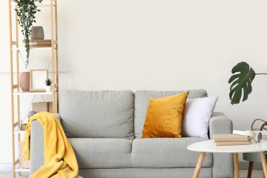 Raf üniteli rahat bir kanepe, sehpa ve oturma odasındaki beyaz duvarın yanında bitkiler.