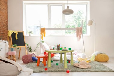 İçinde yatak, dağınık kıyafetler ve oyuncaklar olan dağınık çocuk odası.