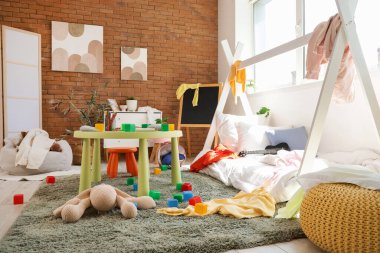 İçinde yatak, dağınık kıyafetler ve oyuncaklar olan dağınık çocuk odası.