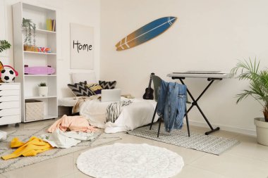 İçinde yatak, sentezleyici ve dağınık giysiler olan dağınık çocuk odası.