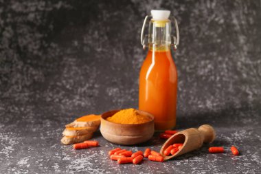 Siyah grunge arka planında bir kase toz, kapsül ve meyve suyu içeren zerdeçal kökü, yakın plan.