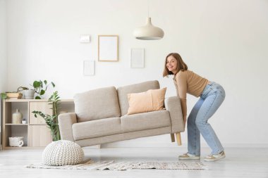 Oturma odasında gri kanepe taşıyan genç bir kadın.