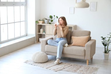 Oturma odasındaki gri koltukta oturan bir fincan kahveyle genç bir kadın.