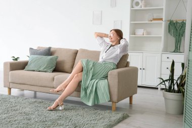 Evdeki gri kanepede dinlenen güzel genç bir kadın.