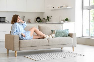 Mutfaktaki gri kanepede yatan genç kadın.