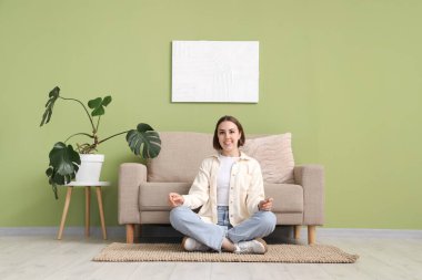 Evdeki gri kanepenin yanındaki halıda oturan genç kadın.