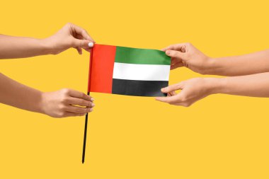 Sarı arka planda BAE bayrağı olan kadın eller