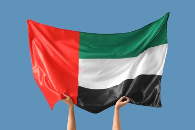 Mavi arka planda BAE bayrağı olan kadın eller