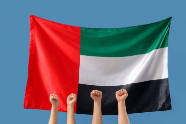 Yumrukları sıkılmış kadın elleri ve mavi arka planda BAE bayrağı