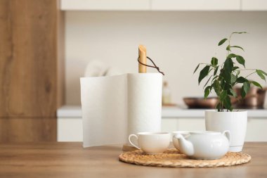 Mutfaktaki masada çay, çaydanlık ve çiçekli kağıt havlu rulosu.