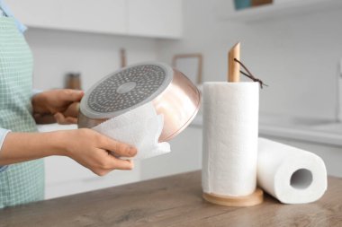 Mutfak masasının yanındaki tavayı temizleyen kağıt havluları olan genç bir kadın.