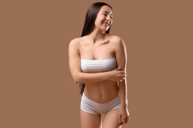 Beyaz iç çamaşırlı, bej arka planda poz veren mutlu genç kadın.