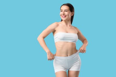 Mavi arka planda beyaz iç çamaşırlı, mutlu genç bir kadın.