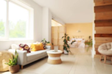 Pencerenin yanındaki kanepe, masa ve modern dizüstü bilgisayarla aydınlatma odasının bulanık görüntüsü