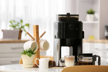 Mutfaktaki yemek masasında fincanlı, fasülyeli ve kremalı modern kahve makinesi.