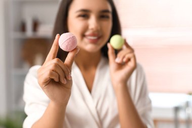 Banyoda banyo bombaları tutan genç ve güzel bir kadın.