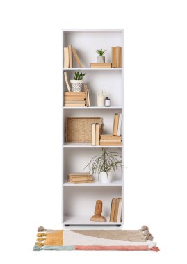 Kitapları, çiçekleri ve beyaz arka planda halısı olan raf ünitesi.