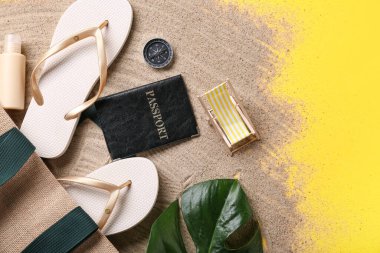 Plaj aksesuarlı pasaport ve sarı arka planda kum.