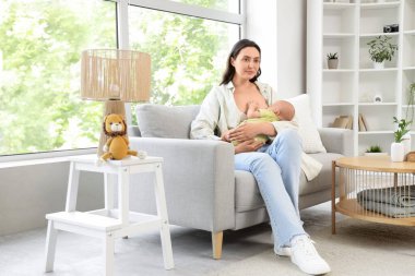 Genç anne bebeğini evdeki kanepede emziriyor.