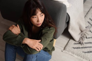 İntihar eğilimli genç Asyalı kadın evinde yerde oturuyor.