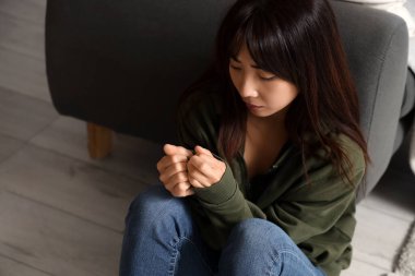 İntihar eğilimli genç Asyalı kadın evinde yerde oturuyor.