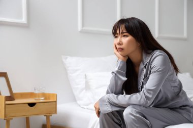 İntihar eğilimli genç Asyalı kadın yatak odasında oturuyor.