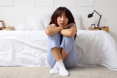 İntihar düşünceleri olan genç bir Asyalı kadın yatak odasında halının üzerinde oturuyor.