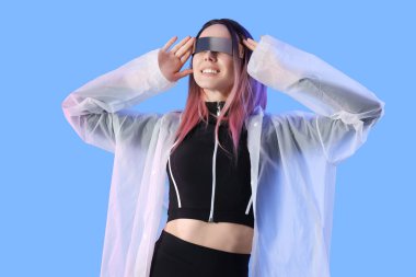 Mavi arka planda VR gözlükleri olan fütürist kostümlü genç bir kadın.