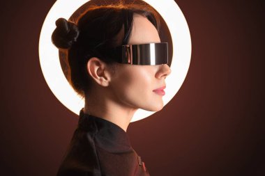 Siyah arka planda parlak halka ışığı olan VR gözlüklü genç kadın, yakın plan.