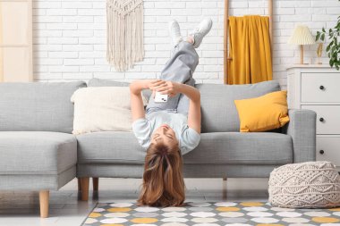 Evdeki gri koltukta cep telefonu kullanan güzel genç bir kadın.